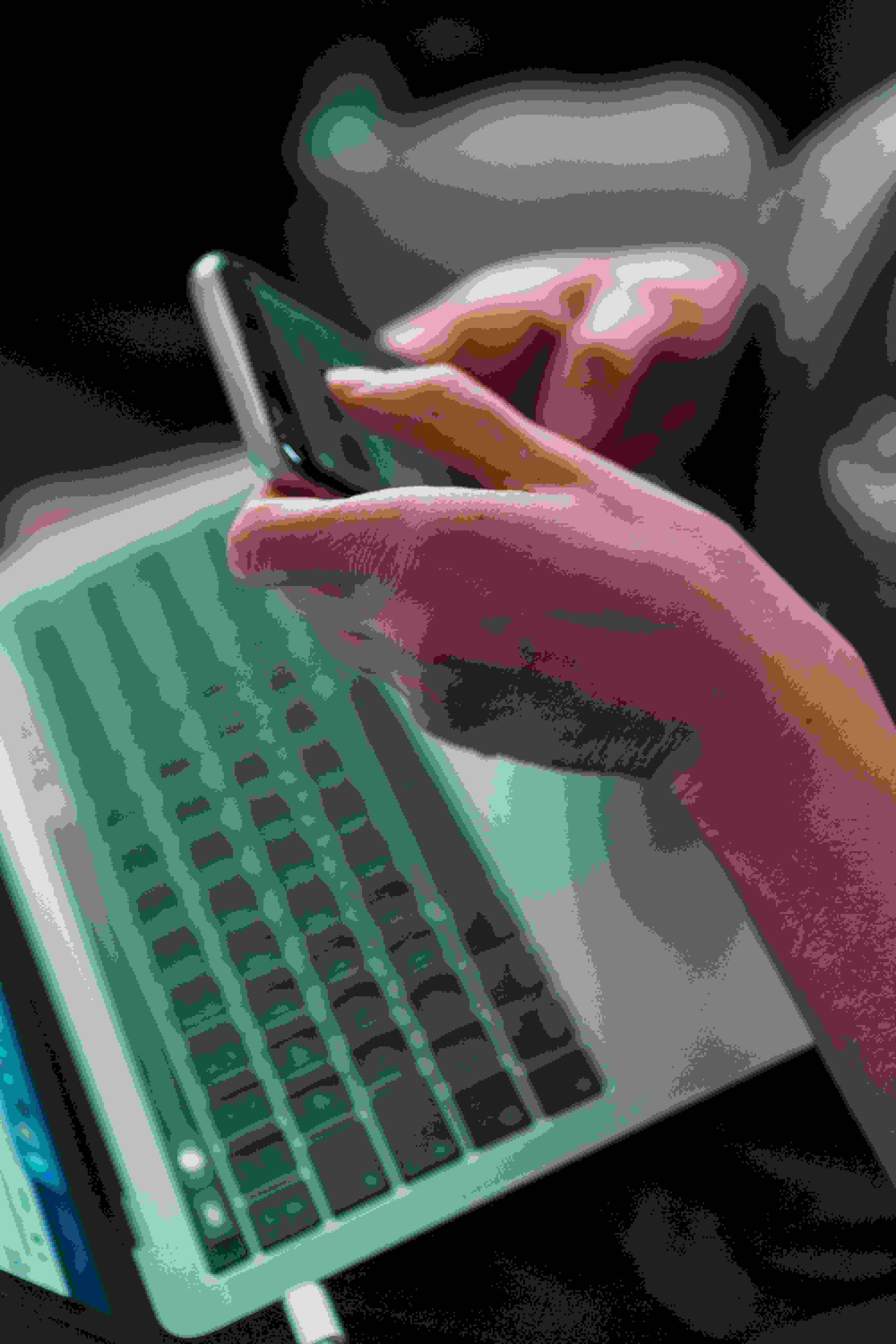 To hænder holder om mobiltelefon med bærbar computer i baggrunden