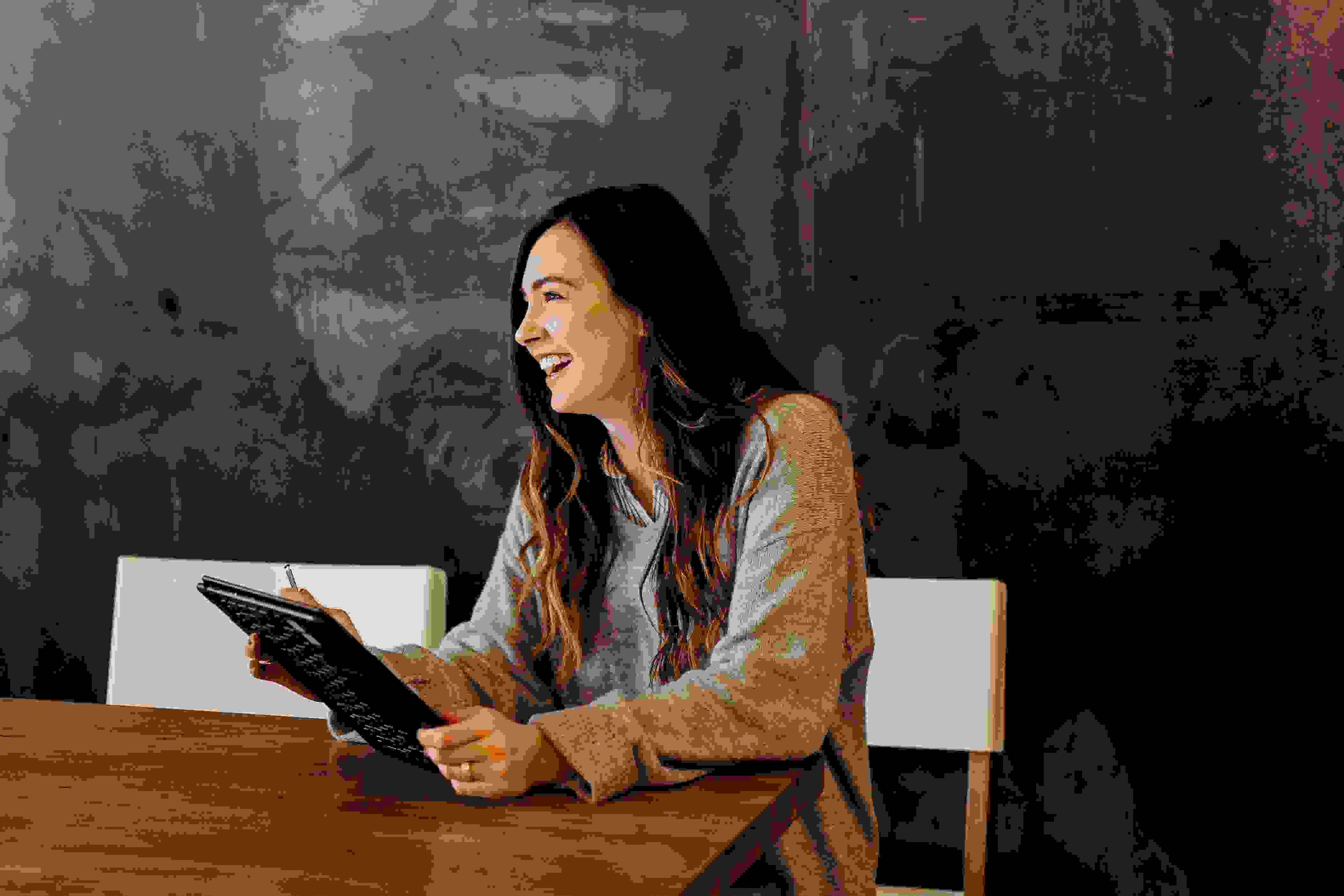 Smilende kvinde sidder ved bord med en tablet i hånden
